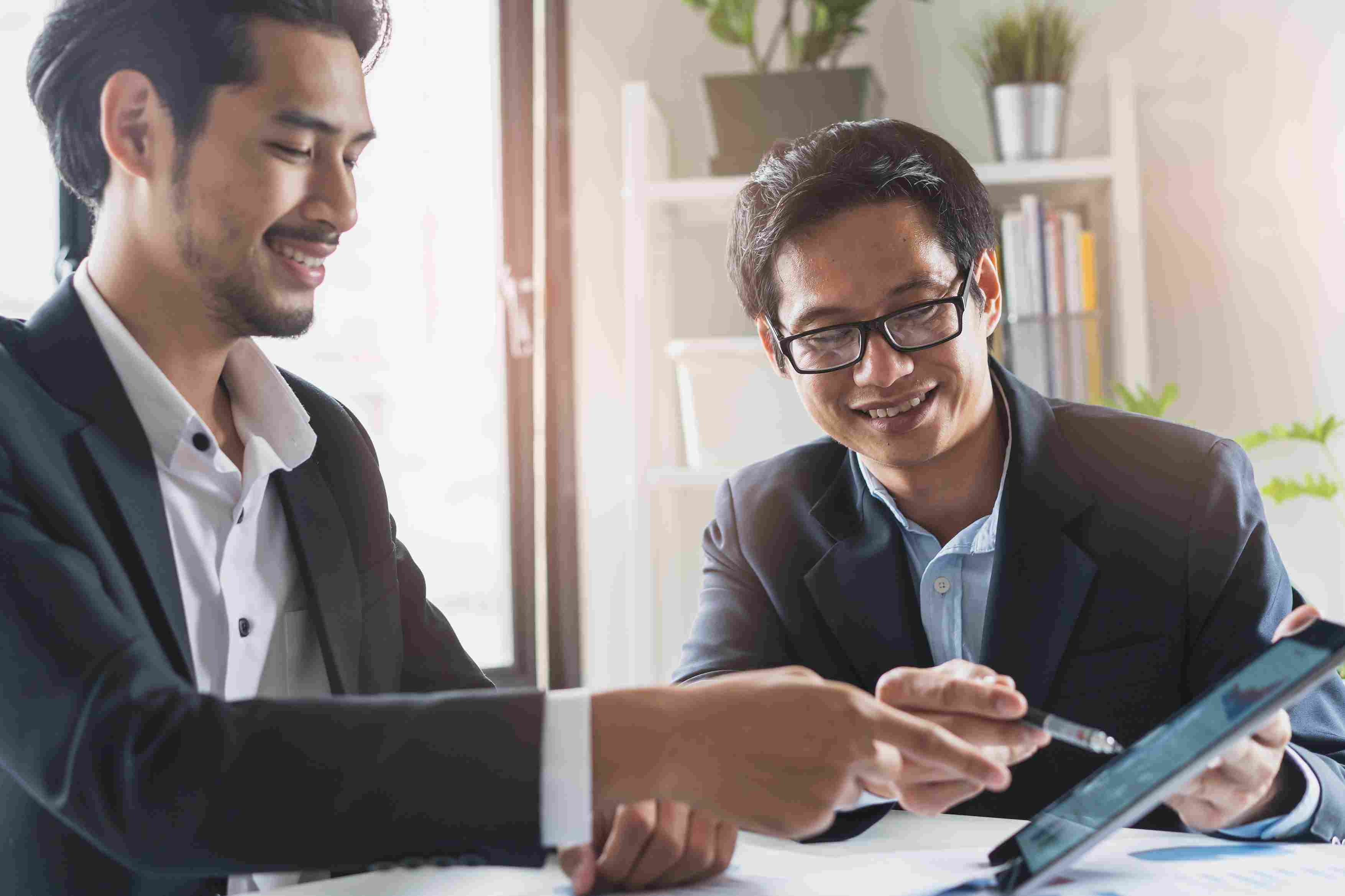 Two individuals discussing business graphs and charts on a tablet in an office room. 